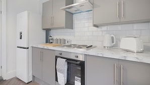 A modern kitchen with grey cabinets, a white refrigerator, a stove, and a coffee maker. - Seaside Haven on Newcomen Grove Redcar Retreat (Redcar)
