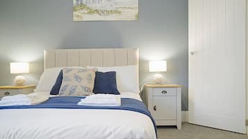 A bedroom with a bed, two bedside tables, a nightstand, a door, and a painting on the wall.