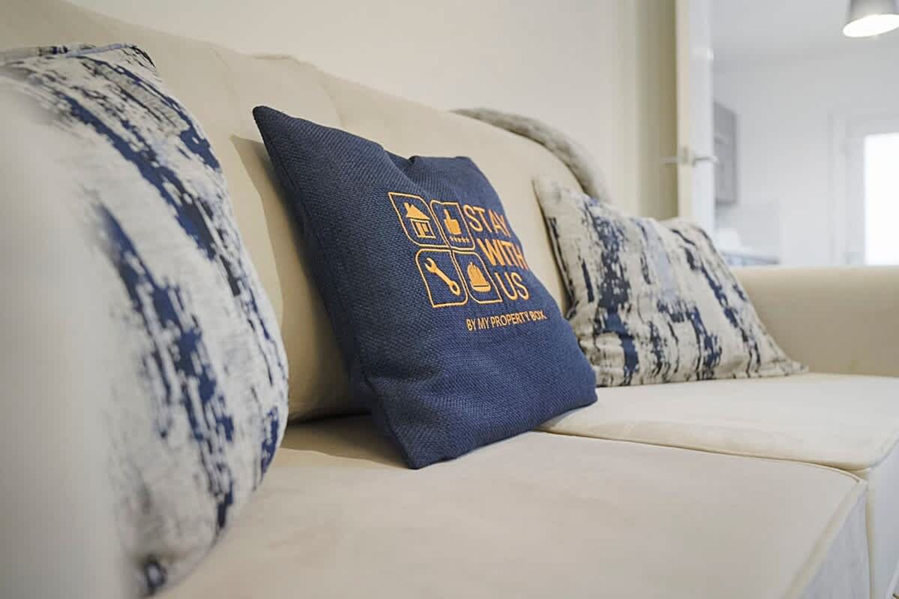 A beige sofa with a dark blue pillow featuring a graphic and text.