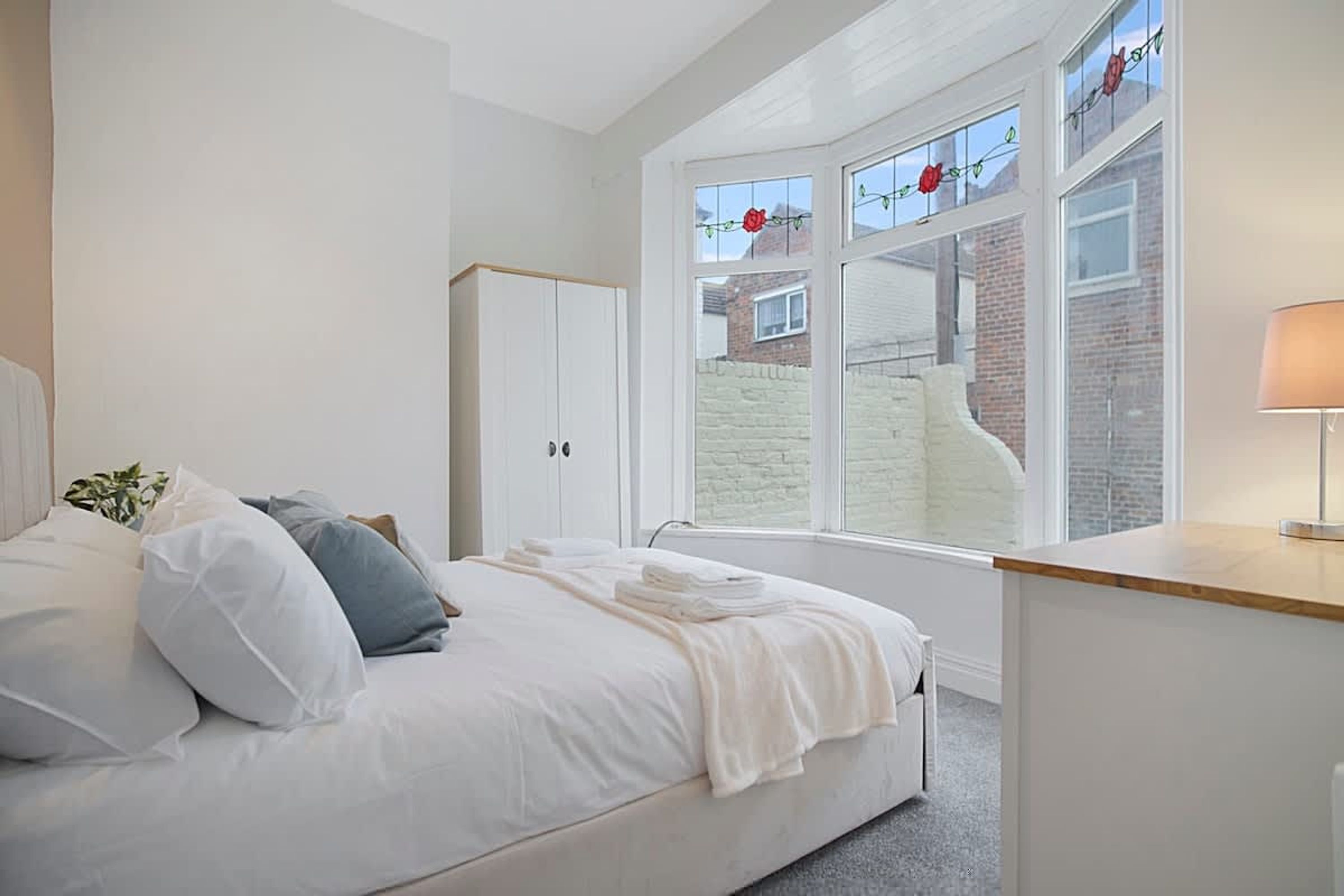 Une chambre à coucher comprenant un lit, une armoire, un bureau et une fenêtre donnant sur un mur de briques et agrémentée d’une décoration florale rouge.