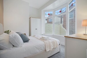 Un dormitorio con cama, armario, escritorio y ventana con vista a una pared de ladrillo y una decoración floral roja.