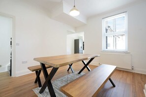 Une cuisine moderne avec une table et un banc en bois, des murs blancs et une fenêtre avec des stores.