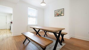 A dining area with a wooden table and bench, a hanging light fixture, and a window with blinds. - Comfortable 4BR Stay Byerley Road by Stay With Us (Shildon)