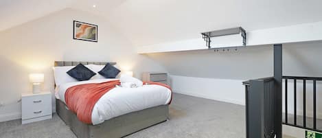 A bedroom with a bed, bedside tables, a nightstand, a ceiling light, a wall-mounted shelf, and a black railing.