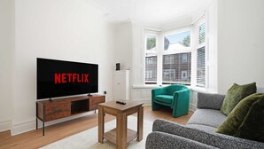 A living room with a television displaying 'NETFLIX,' a wooden coffee table, a teal armchair, and a grey sofa. - Comfortable 4BR Stay Byerley Road by Stay With Us (Shildon)