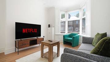A living room with a television displaying 'NETFLIX,' a wooden coffee table, a teal armchair, and a grey sofa.