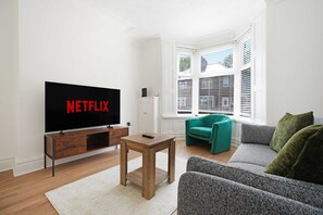 A living room with a television displaying 'NETFLIX,' a wooden coffee table, a teal armchair, and a grey sofa. - Comfortable 4BR Stay Byerley Road by Stay With Us (Shildon)