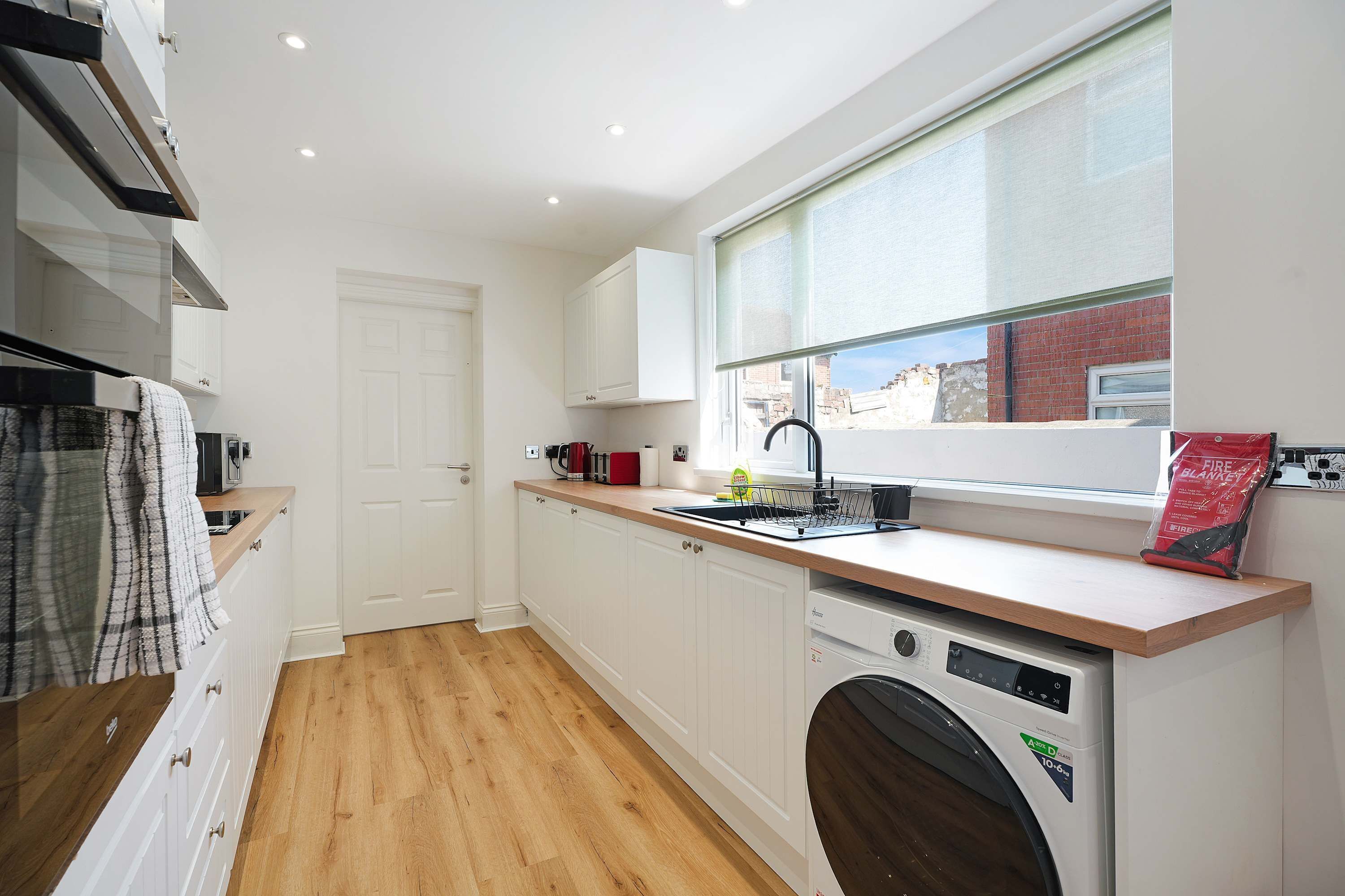 A compact kitchen with a built-in dishwasher, a window with a view of the outside, and a wooden floor.
