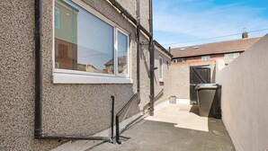 A narrow alleyway with a house on one side and a garage on the other. There are visible pipes and a window on the house. - Comfortable 4BR Stay Byerley Road by Stay With Us (Shildon)