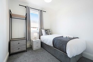 Une chambre à coucher avec un lit, des tables de chevet, un miroir et une vue sur l’extérieur.