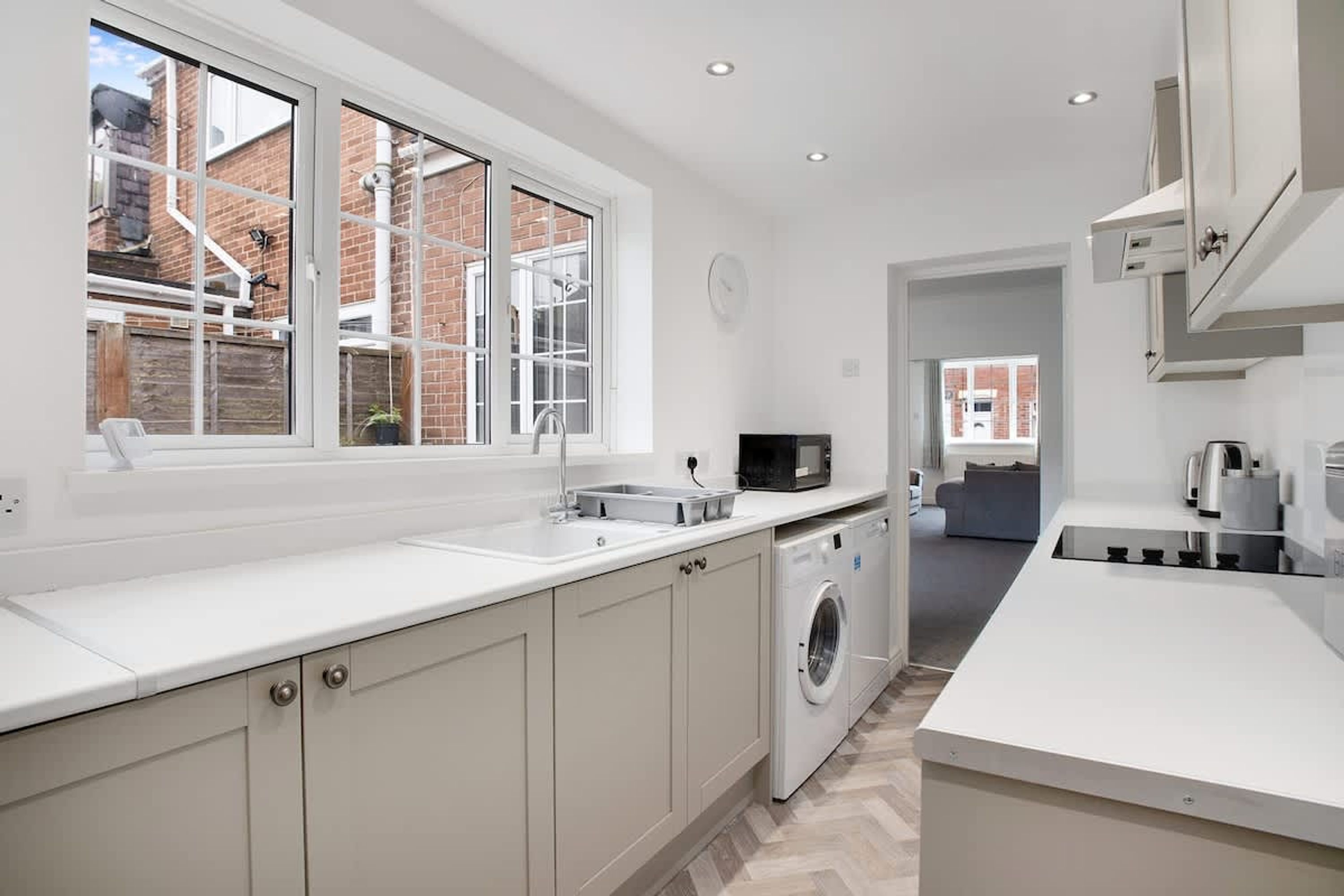 A modern kitchen with a built-in washing machine, a microwave, and a large window.