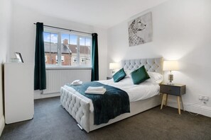 A bedroom with a bed, bedside tables, a window, and a radiator. - Comfortable Three Bedroom Family Apartment (Houghton le Spring)