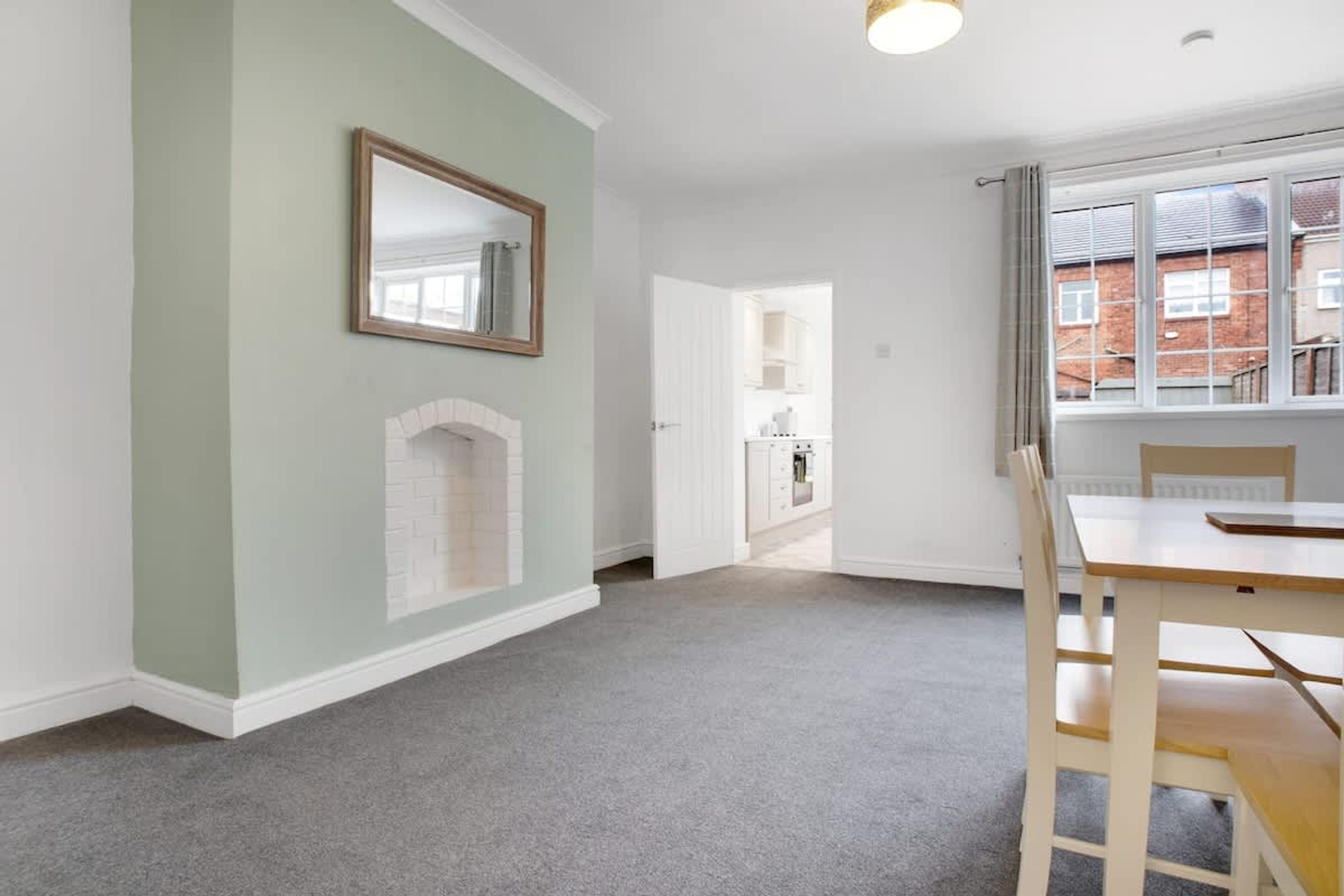 A room with a fireplace, a dining table with chairs, a mirror on the wall, and a window with a view of buildings.