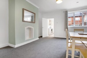 Une pièce avec une cheminée, une table à manger avec des chaises, un miroir au mur et une fenêtre donnant sur des immeubles.