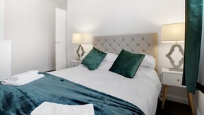Una cama bien hecha con un edredón blanco y verde azulado, dos almohadas verdes y una manta verde azulado a juego.
