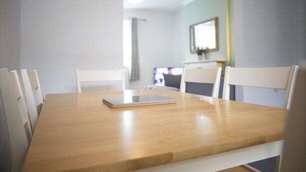Una mesa de comedor con sillas, una tableta y vista a una cocina.