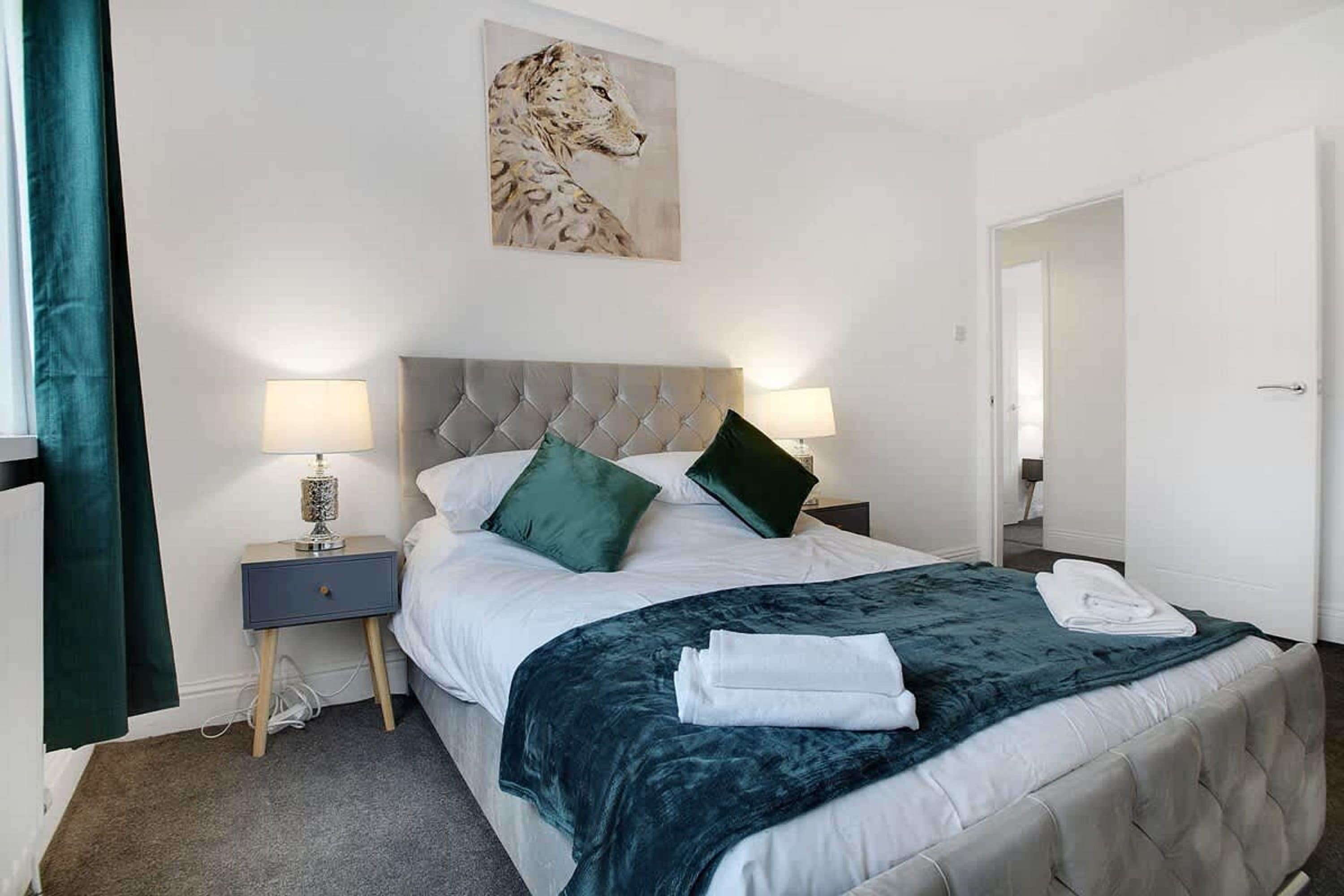 A hotel room with a bed, two bedside lamps, a painting of a leopard, and a door.