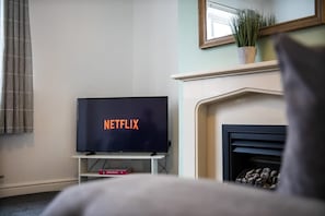 A living room with a television displaying 'NETFLIX' on the screen, a fireplace, and a plant on the mantel. - Comfortable Three Bedroom Family Apartment (Houghton le Spring)