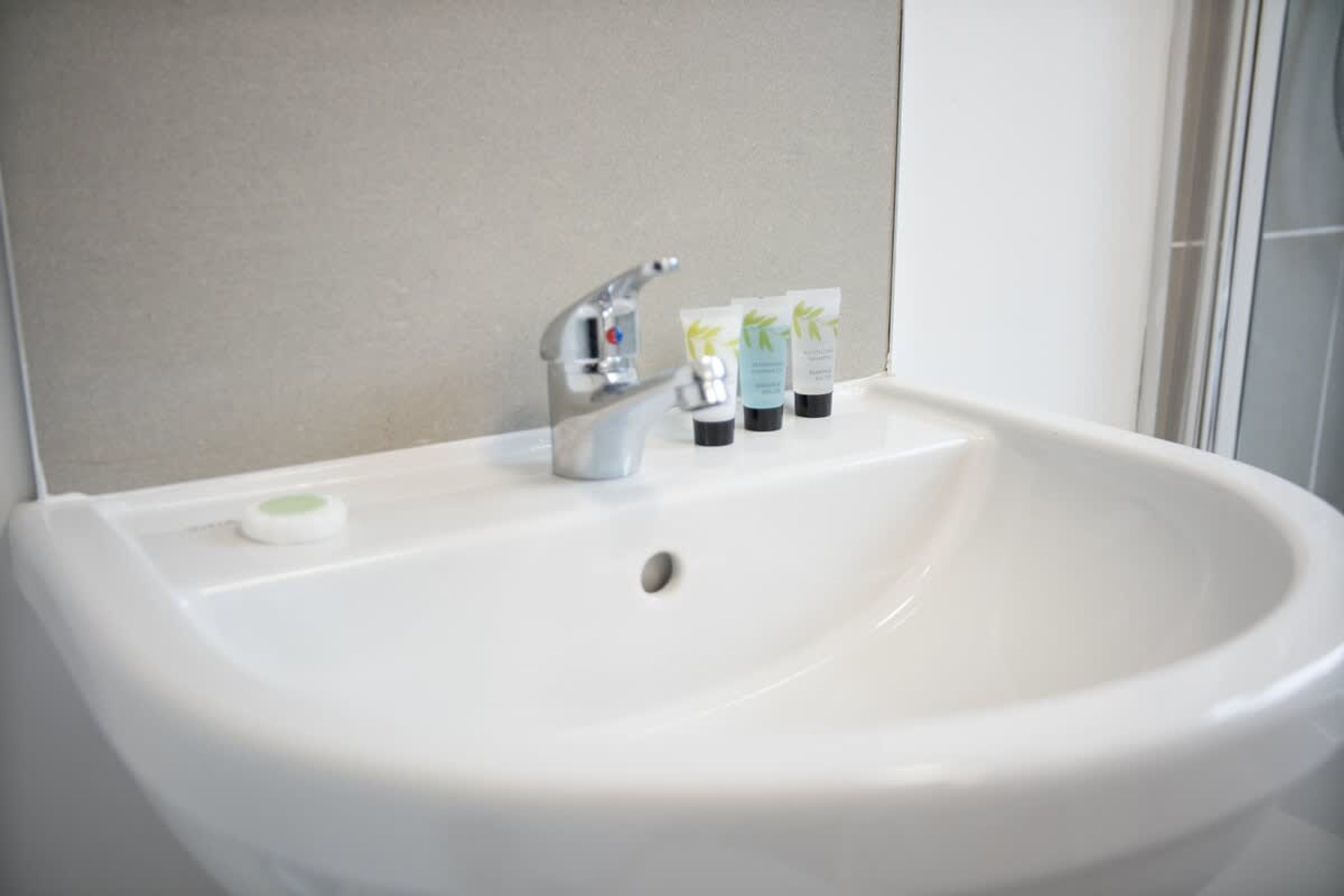 A white bathroom sink with a silver faucet, a soap dish, and three toiletry bottles.