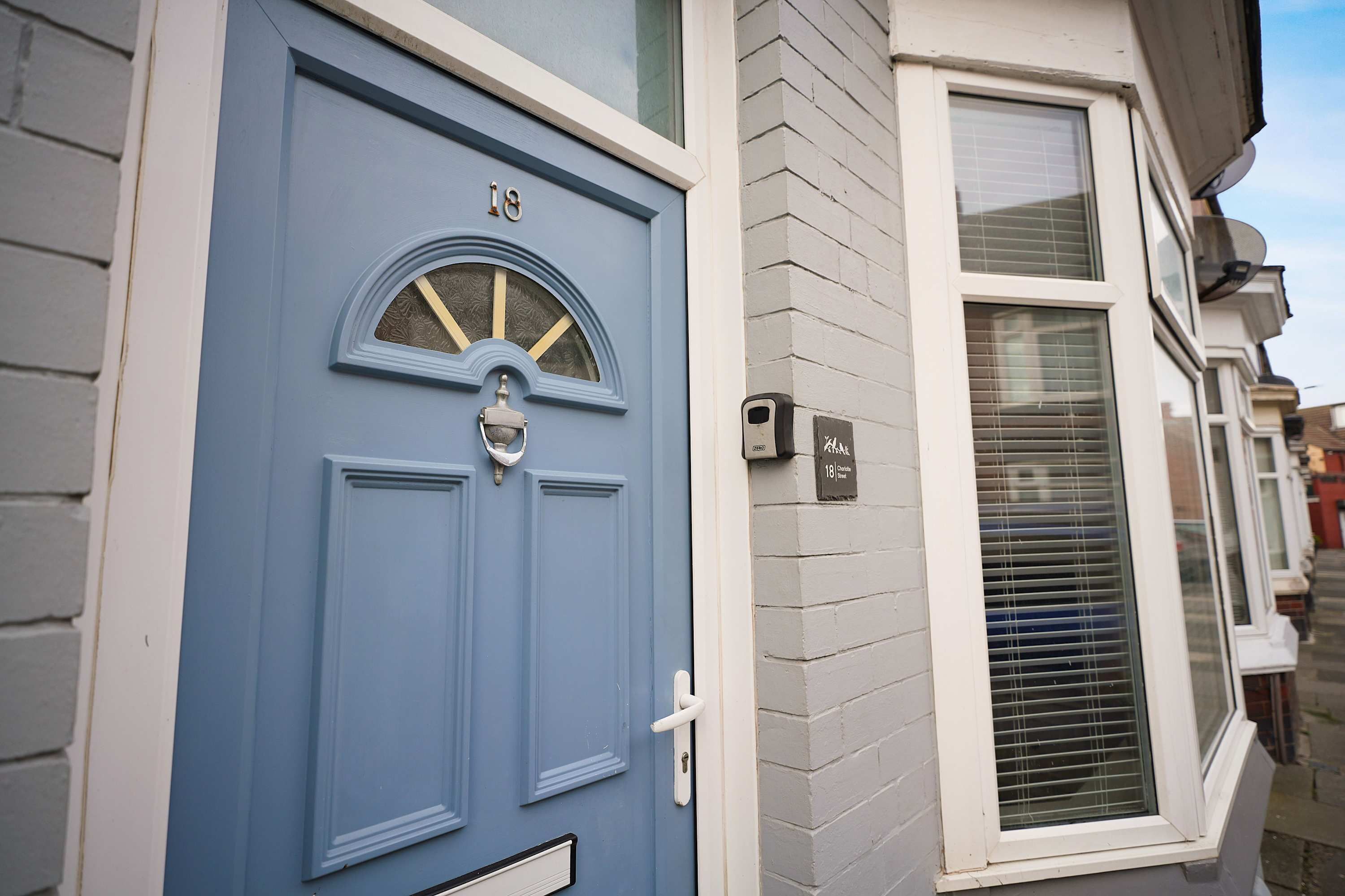A blue door with a number plate, a white window with blinds, and a small outdoor light fixture.