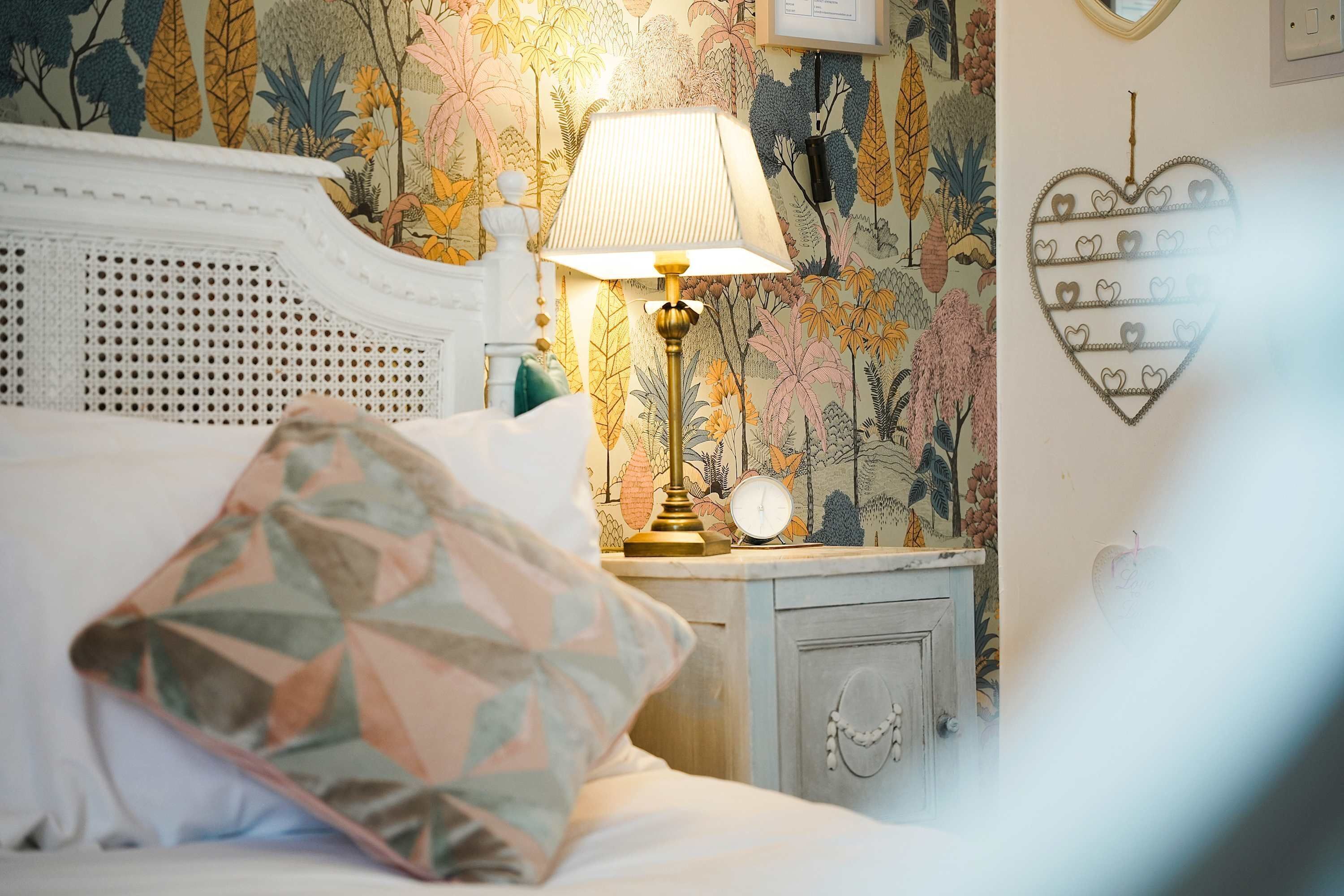 A neatly made bed with a patterned pillow, a bedside lamp, and a wall clock on a nightstand.