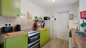 A kitchen with green cabinets, a stove, a microwave, and a clock on the wall. - Charming 3 Bed Steps From Redcar Beach and Station (Redcar)