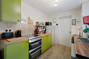 A kitchen with green cabinets, a stove, a microwave, and a clock on the wall. - Charming 3 Bed Steps From Redcar Beach and Station (Redcar)