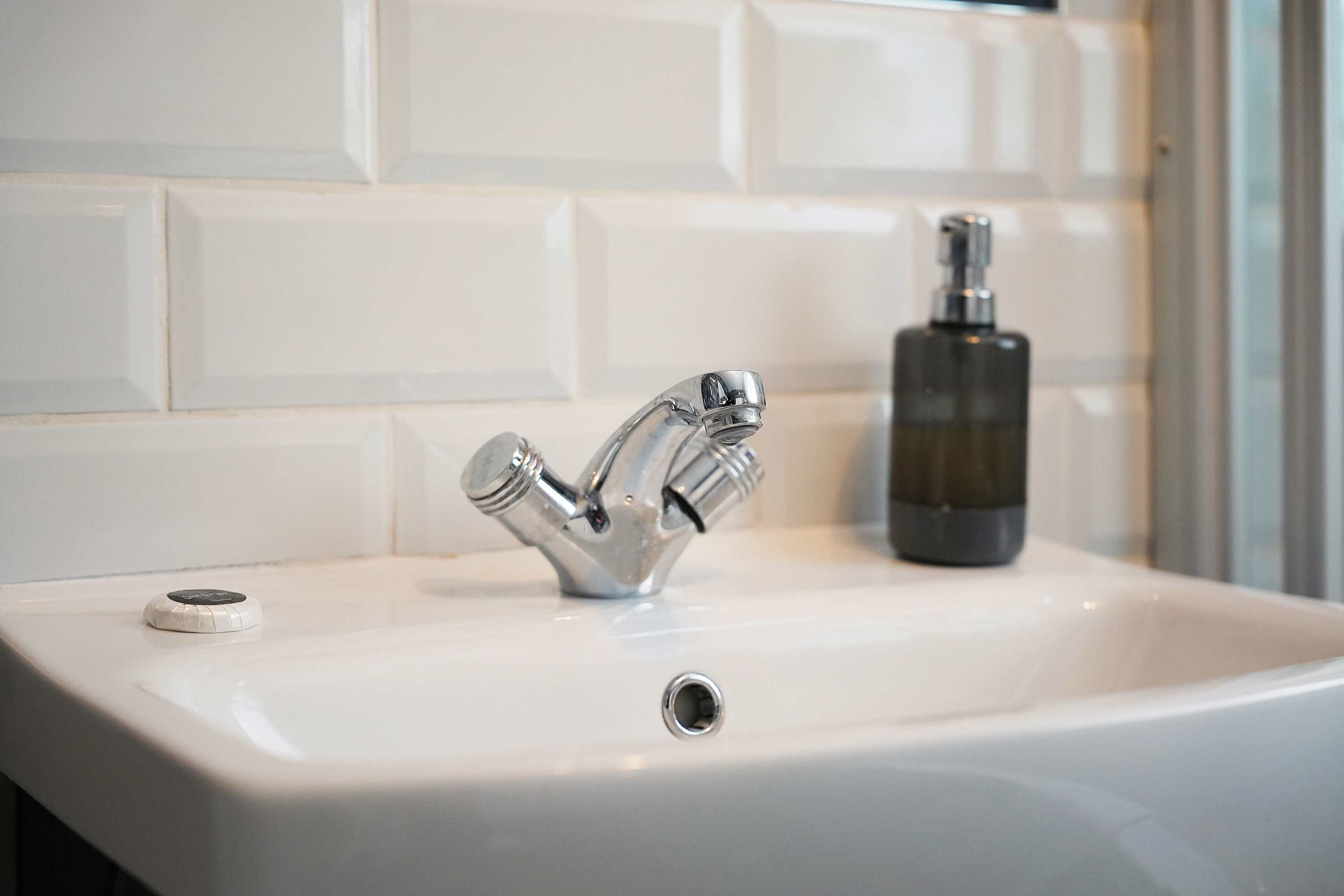 Ein Badezimmerwaschbecken mit einem modernen Wasserhahn und einer Seifenspender.