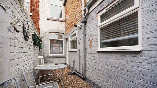 A narrow outdoor space with a metal table and chairs, a lantern, and a brick wall. - Charming 3 Bed Steps From Redcar Beach and Station (Redcar)