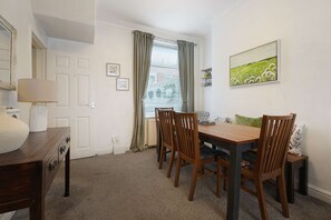 A dining area with a wooden table and chairs, a lamp, a radiator, and a window with curtains. - Charming 3 Bed Steps From Redcar Beach and Station (Redcar)