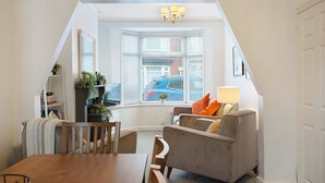 A cozy attic room with a dining table, a sofa, and a bay window with blinds. - Charming 3 Bed Steps From Redcar Beach and Station (Redcar)