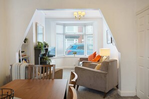 A cozy attic room with a dining table, a sofa, and a bay window with blinds. - Charming 3 Bed Steps From Redcar Beach and Station (Redcar)