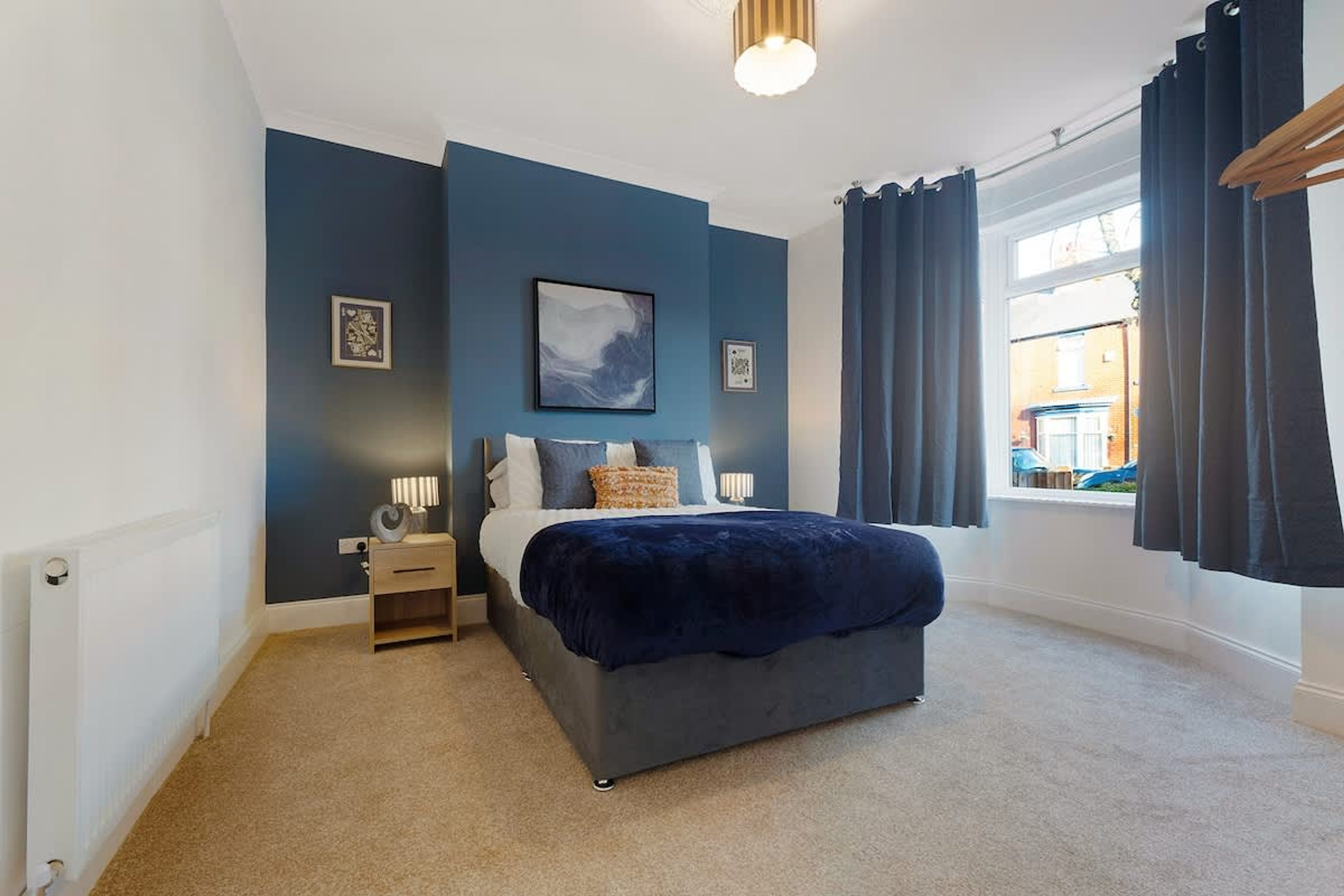 A bedroom with a bed, bedside tables, a window with curtains, and artwork on the walls.