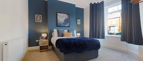 A bedroom with a bed, bedside tables, a window with curtains, and artwork on the walls.