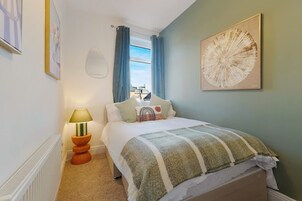 Un dormitorio con cama, lámpara, ventana con cortinas y una obra de arte en la pared.