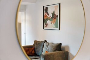 Ein Zimmer mit einer Couch, einem gerahmten abstrakten Gemälde an der Wand und einer Tür zu einem weiteren Raum.