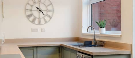 A modern kitchen with a built-in dishwasher, a window with a view of a brick wall, and a wall-mounted clock.