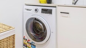 Un lavadero compacto y moderno con lavadora de carga frontal, un lavamanos pequeño y una cesta de mimbre.