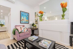 Ein modernes Wohnzimmer mit einer Couch, einem Couchtisch mit Zeitschriften, einem gerahmten Bild von Melbourne und einer Vase mit Blumen.