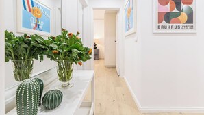 Un pasillo con obras de arte en las paredes, una mesa blanca con jarrones y adornos, y una puerta que da a otra habitación.