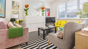Una sala de estar moderna con un sofá, un sillón y una mesita de centro. Hay un televisor y una ventana con persianas.