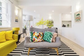 Ein modernes Wohnzimmer mit grauem Sofa, gelbem Sessel und einem schwarz-weißen Teppich.
