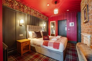 Een hotelkamer met een bed, nachtkastje en een roodruitig vloerkleed.