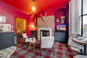Een kamer met een open haard, een televisie en een eethoek met een geruit tapijt.