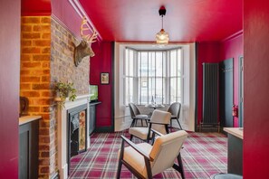 A room with a fireplace, a red brick wall, a plaid carpet, and a dining area with chairs and a table. - Boutique 1 Bedroom in Hartlepool With Fireplace (Hartlepool)