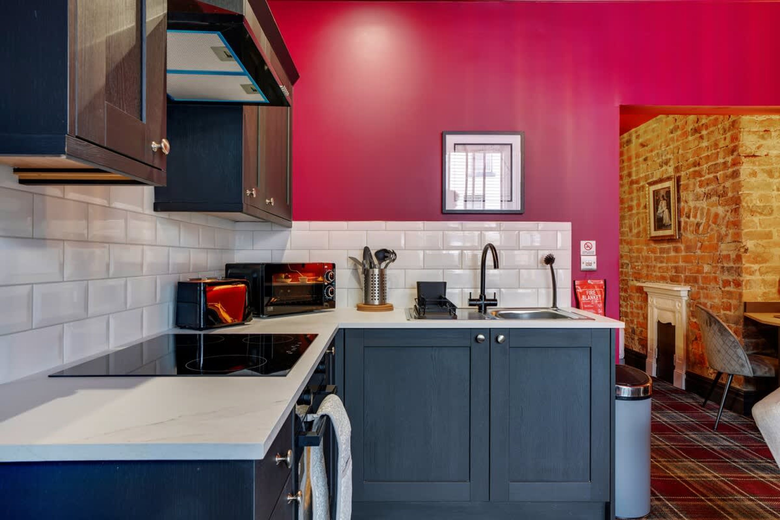 A modern kitchen with a central island, white subway tiles, a red accent wall, and a brick fireplace.