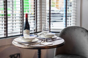 A table set with a bottle of wine, two glasses, and plates, positioned by a window with blinds. - Boutique 1 Bedroom in Hartlepool With Fireplace (Hartlepool)