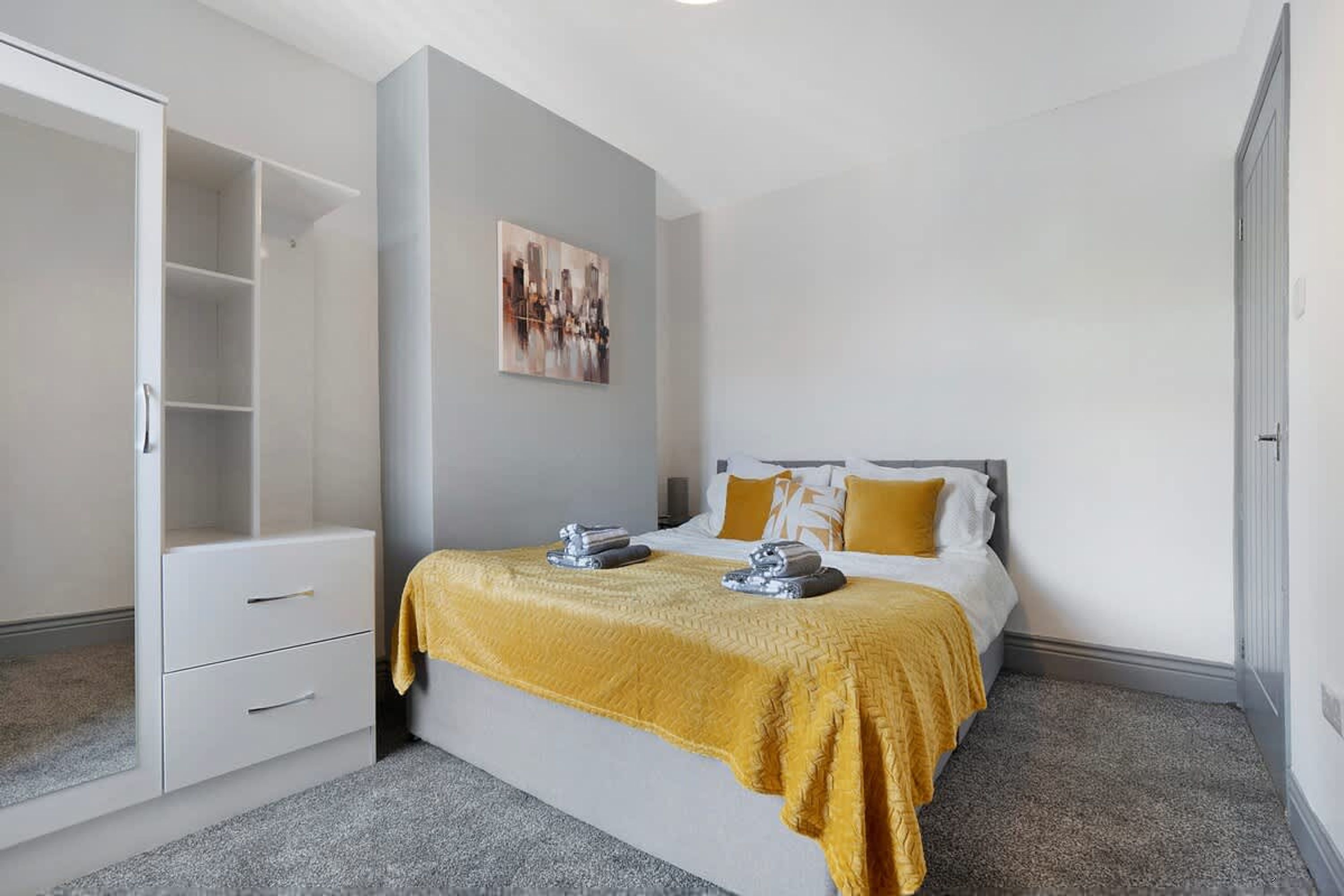 A hotel room with a bed, a wardrobe, and a painting on the wall.