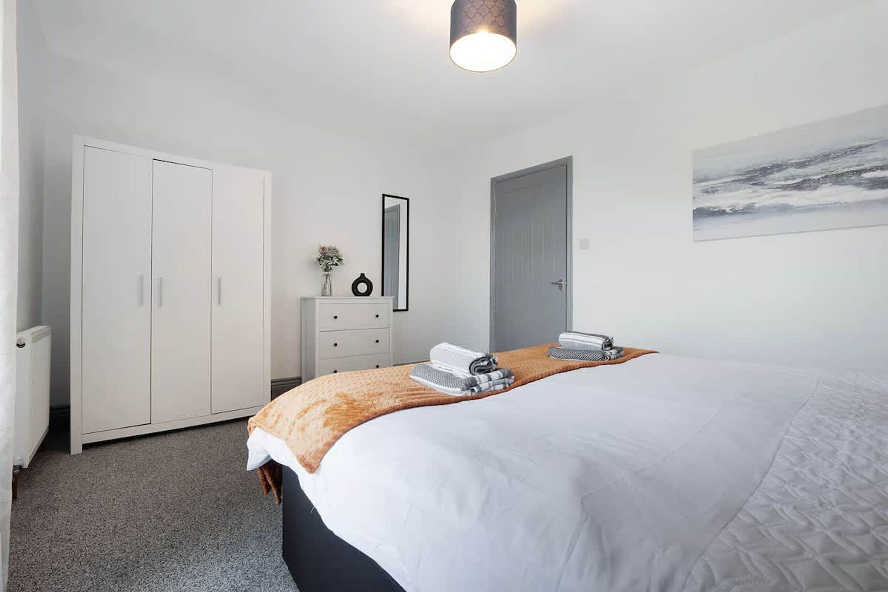 A bedroom with a bed, a dresser, a wardrobe, a mirror, and a painting on the wall.