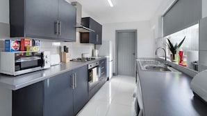 Cozinha moderna com armários escuros, forno embutido, micro-ondas e pia de aço inoxidável.